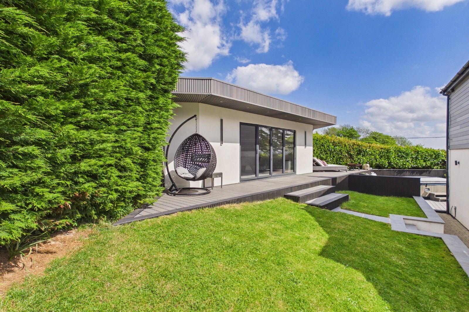 White-render garden room, dark slatted soffit, composite deck