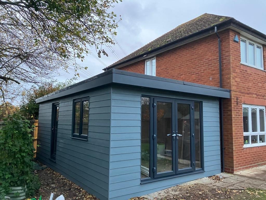 Grey-blue clad garden room beside a brick house